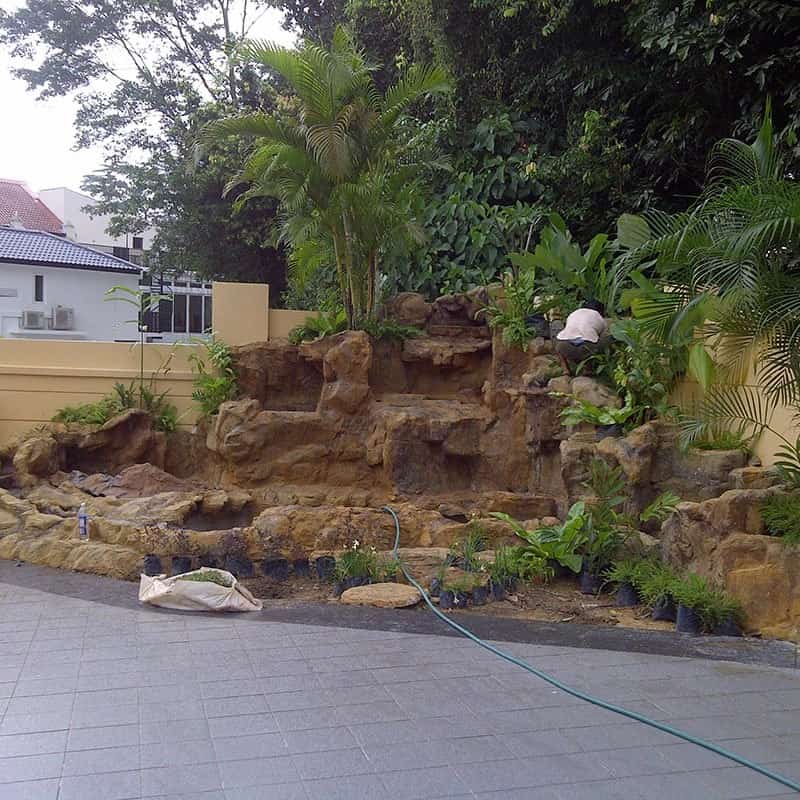 Rock waterfall and pond under construction with a crew member setting out plants