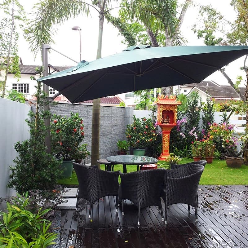 Timber deck with rattan dining set under a cantilever umbrella beside turf and flowering shrubs